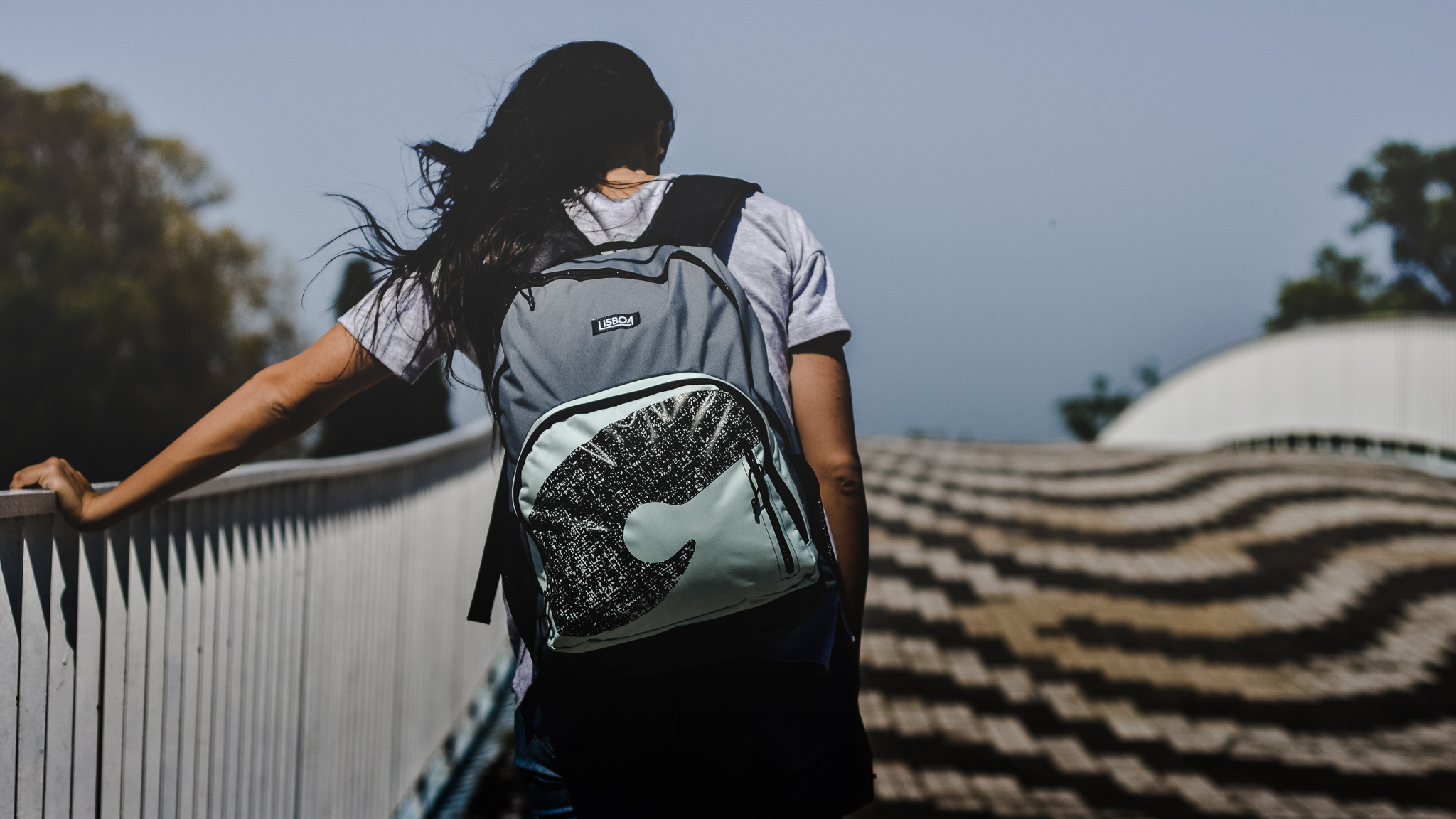 A woman with a backpack strolling on a bridge, enjoying the scenic view.