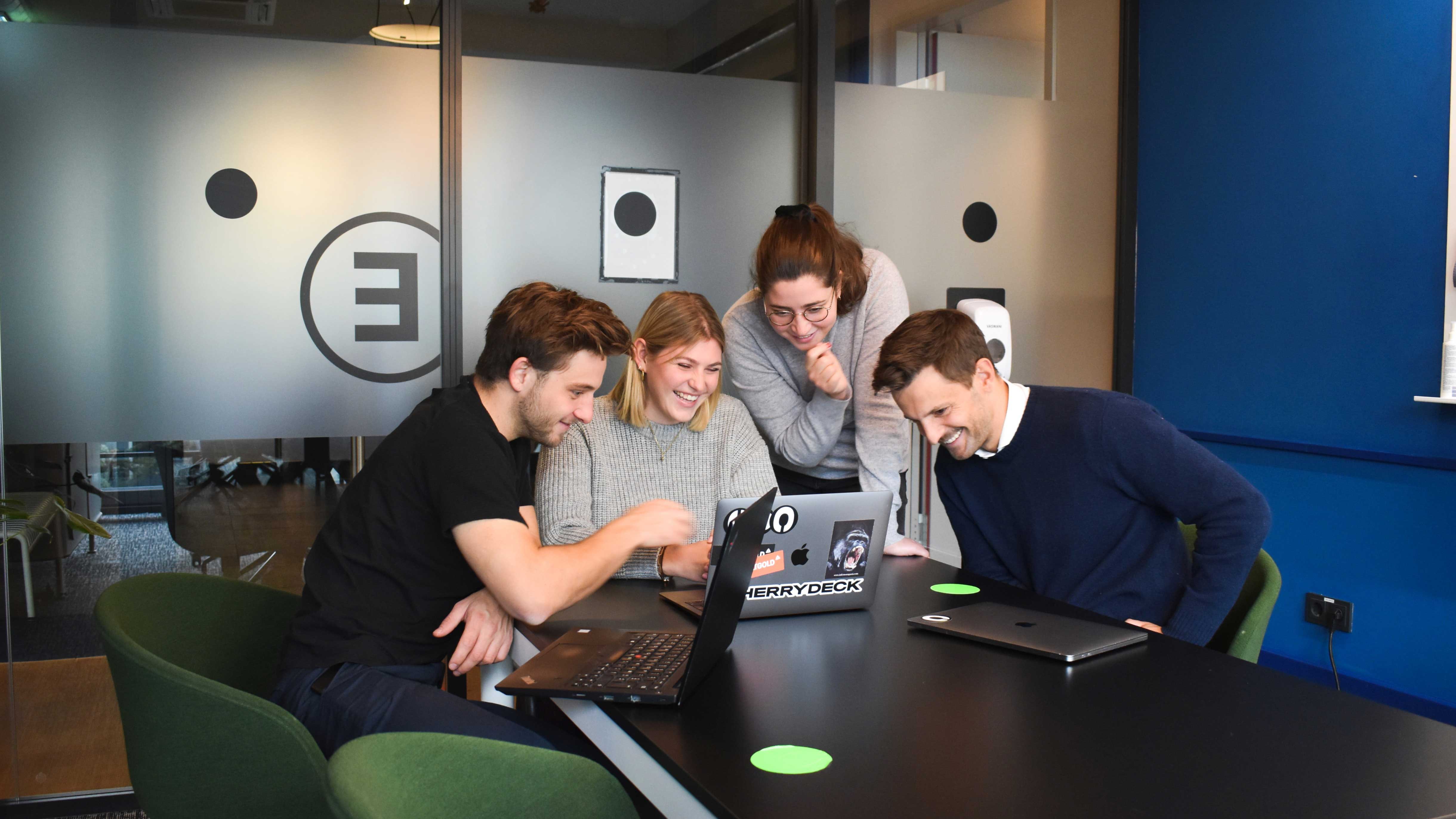 A group of four people working together around an office table with their notebooks.