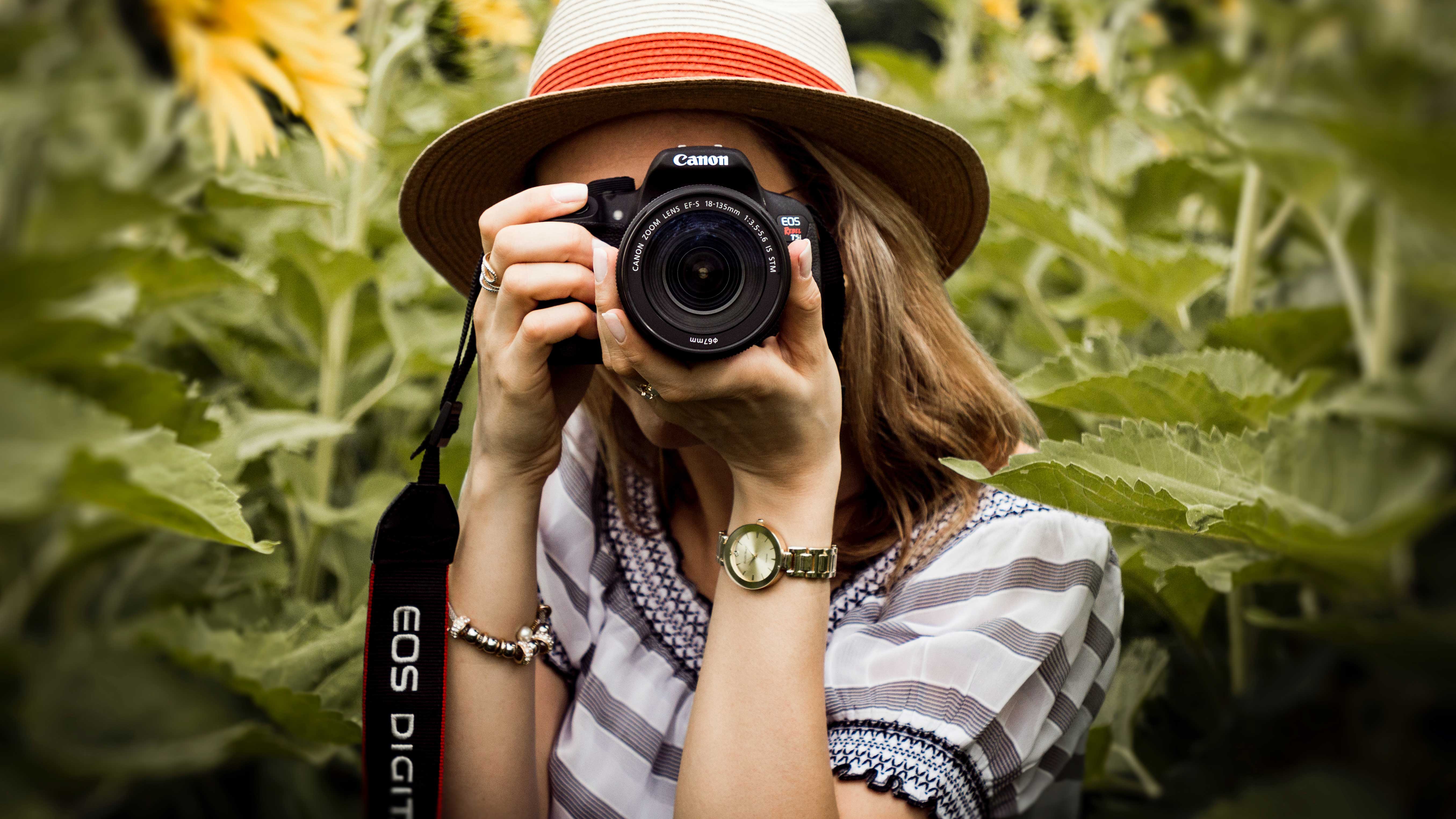 A woman with the camera at hand taking a picture around a field of sunflowers.