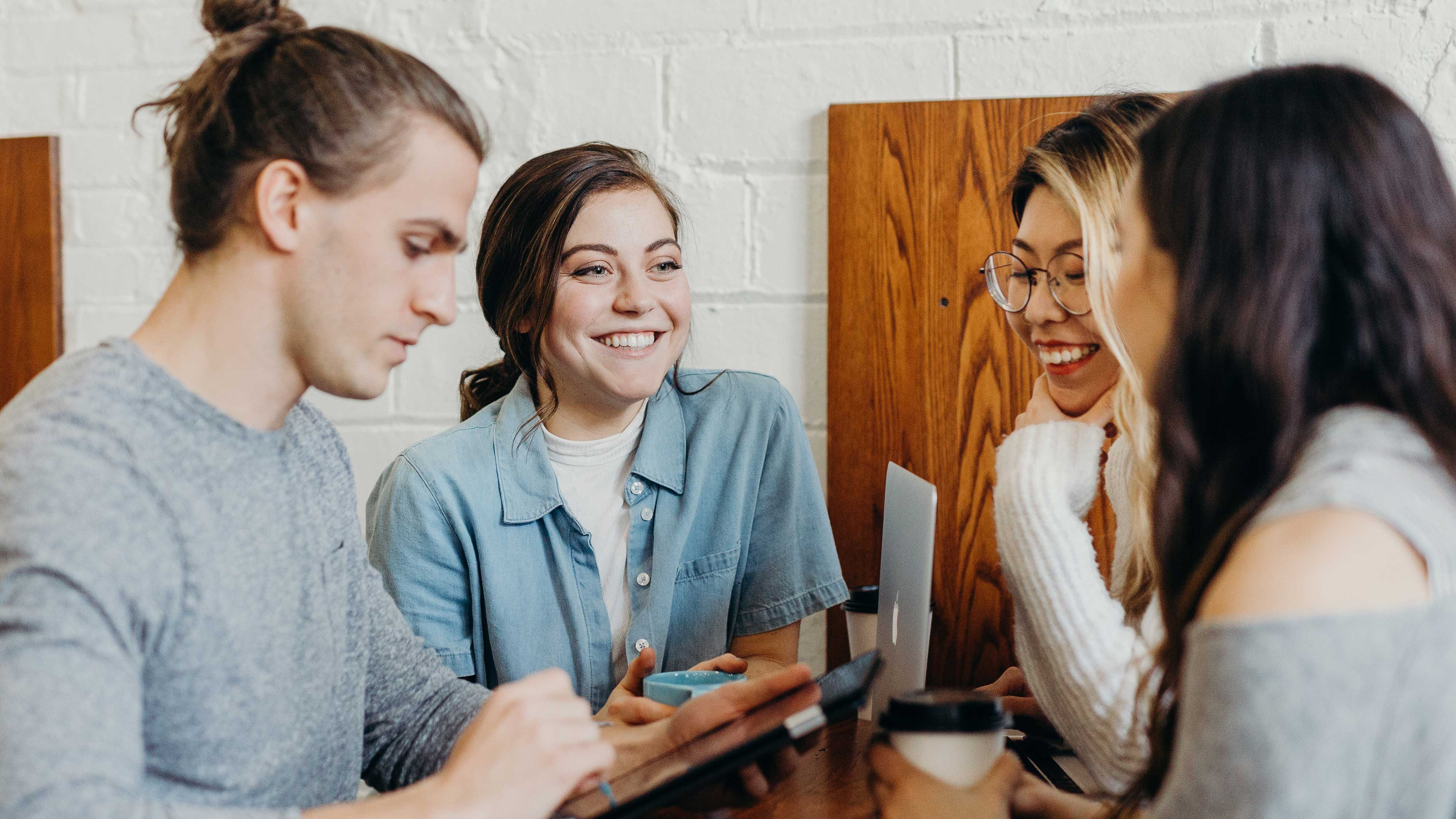 A group of four people working together while they smile and have coffee together.